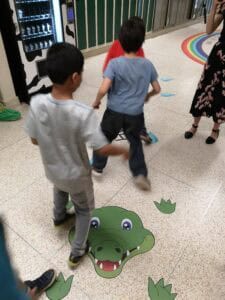 Children playing on sensory path with crocodile design in indoor setting.