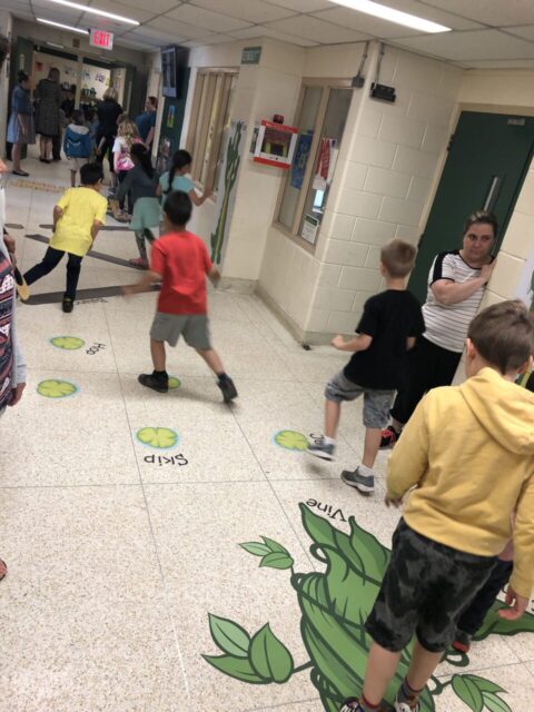 Children playing on sensory paths with colorful footprints and leaf designs in school hallway.